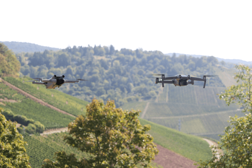 Die DJI Mini 3 Pro und die DJI Air 2S schweben nebeneinander und halten sich waagrecht in der Luft.